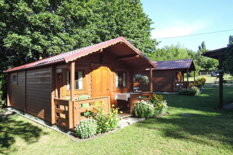 Wooden cabin with covered porch, surrounded by flowers and greenery, Bungalows Lubin Type A Jolanta, Germany.