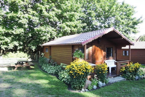 Charming wooden cabin surrounded by greenery, yellow flowers, a white chair, and a picnic table in Germany.