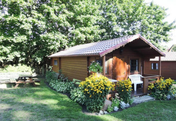 Encantadora cabaña de madera con jardín, flores amarillas, silla blanca y mesa de picnic en Alemania.