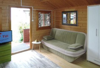 Accogliente soggiorno in bungalow di legno con divano, TV, specchio, tavolino e armadio in Germania.