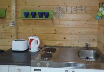 Pequeña cocina de madera con fregadero, cocina, hervidor, tostadora y tazas en Bungalows Lubin Type A Jolanta.