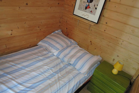 Cozy wooden cabin bedroom with single bed, striped bedding, green nightstand, and yellow lamp at Bungalows Lubin Type A Jolanta.