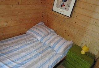 Accogliente camera da letto in legno con letto singolo, comodino verde e lampada gialla ai Bungalows Lubin Type A Jolanta.
