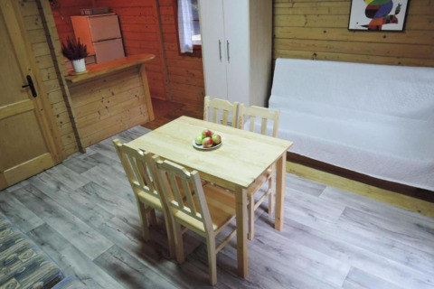 Vue intérieure d'un bungalow en bois avec table à manger, quatre chaises, canapé, armoire et petite cuisine.