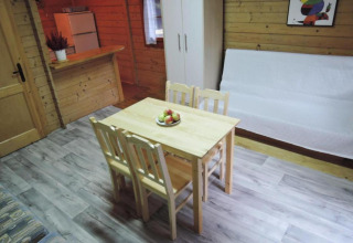Vue intérieure d'un bungalow en bois avec table à manger, quatre chaises, canapé, armoire et petite cuisine.