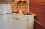 Kleine Küchenzeile in einer Holz-Bungalow, mit weißem Kühlschrank, Spüle, Herd und bunten Tassen.