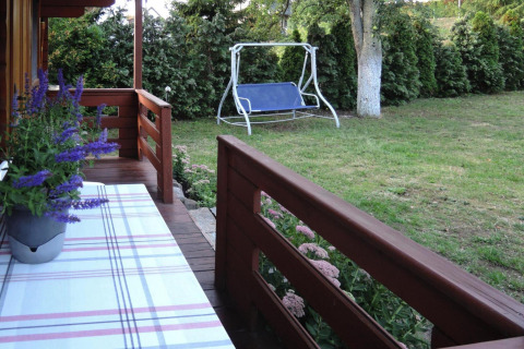 Veranda in legno con fiori, tavolo e vista sul giardino con altalena a Bungalows Lubin Type A Jolanta.