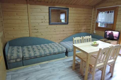 Cozy cabin interior with two sofas, table, four chairs, window, and TV at Bungalows, Lubin-Type B, Germany.