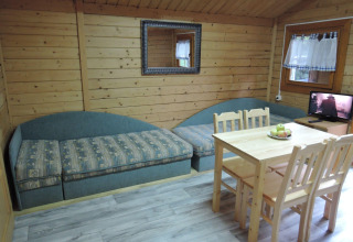 Cozy cabin interior with two sofas, table, four chairs, window, and TV at Bungalows, Lubin-Type B, Germany.