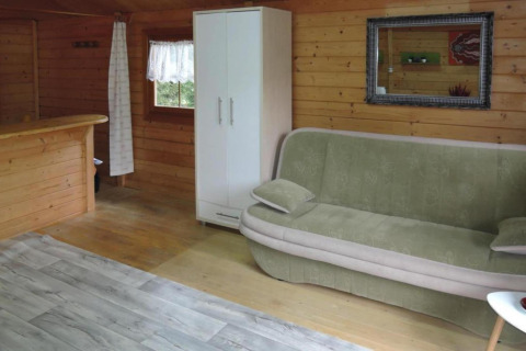 Interior of a wooden cabin with a green sofa, white wardrobe, mirror, window, and partial bar in Germany.