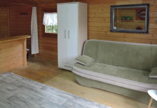 Interior of a wooden cabin with a green sofa, white wardrobe, mirror, window, and partial bar in Germany.