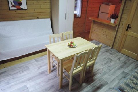 Intérieur de bungalow en bois avec table à manger, quatre chaises, canapé, armoire et réfrigérateur.