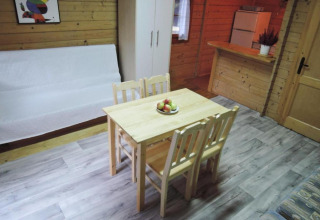 Cozy bungalow interior with wooden walls, dining table, four chairs, sofa, wardrobe, and fridge.
