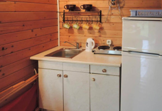 Compact wooden cabin kitchenette with sink, stove, electric kettle, cups, and fridge in Germany.