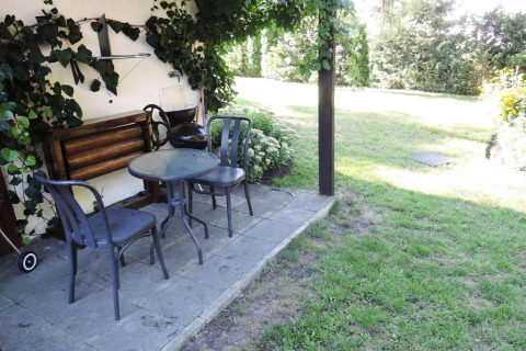 Outdoor patio area with two metal chairs and a round glass table next to a lush garden at a cabin.