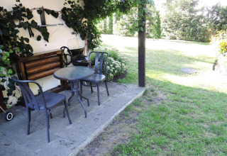 Outdoor patio area with two metal chairs and a round glass table next to a lush garden at a cabin.