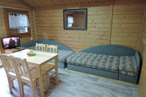 Living room of a wooden cabin with a dining table, four chairs, two sofas, TV, and a wall mirror.
