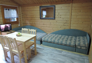 Living room of a wooden cabin with a dining table, four chairs, two sofas, TV, and a wall mirror.