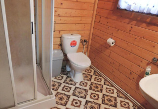 Salle de bain en cabine boisée avec douche, toilettes, lavabo, sol à motifs et fenêtre avec rideau.