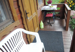Véranda en bois d’un chalet avec banc blanc, porte jaune, table, tabouret rouge et fleurs au jardin.