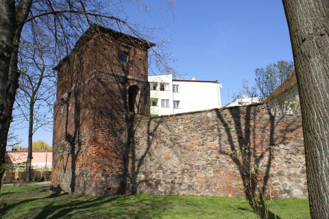 Vecchia torre e muro di pietra al sole, con edifici moderni e alberi sullo sfondo in Germania.