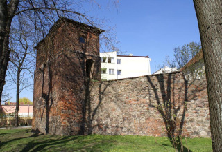 Vecchia torre e muro di pietra al sole, con edifici moderni e alberi sullo sfondo in Germania.