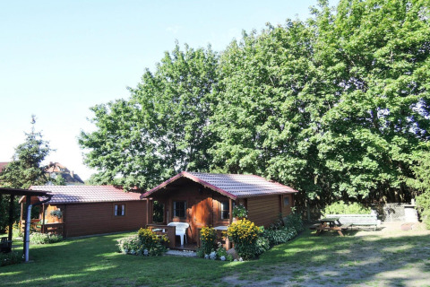 Wooden bungalow with red roof surrounded by green trees, flowers, and sunshine in Germany.