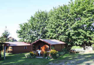 Wooden bungalow with red roof surrounded by green trees, flowers, and sunshine in Germany.