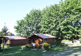 Bungalow de madera con techo rojo rodeado de árboles y flores verdes bajo el sol en Alemania.