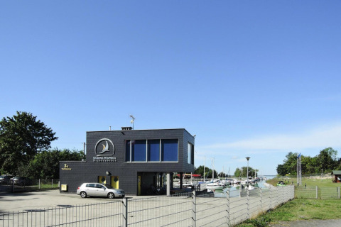 Bâtiment noir de Marina Warpoes avec voiture, bateaux et espaces verts sous ciel bleu en Allemagne.