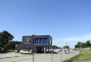 Bâtiment noir de Marina Warpoes avec voiture, bateaux et espaces verts sous ciel bleu en Allemagne.