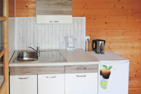 Pequeña cocina en una cabaña de madera con fregadero, hervidor eléctrico, jarra y mini nevera.