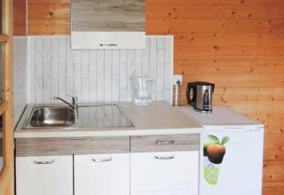 Pequeña cocina en una cabaña de madera con fregadero, hervidor eléctrico, jarra y mini nevera.