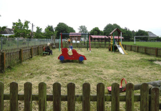 Fenced playground area with children playing on equipment, a slide, and adults sitting on benches nearby.