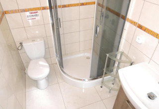 Baño luminoso con ducha, inodoro, lavabo y estante de vidrio en la cabaña At słonecznikiem en Alemania.