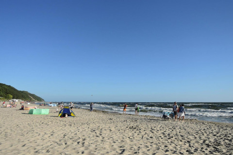 Personas disfrutan de un día soleado en una playa con olas y cielo azul cerca de At «słonecznikiem» en Alemania.