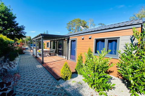 Buitenfoto van een hedendaagse glamping accommodatie met houten terras, tuin en zitbank in de zon.