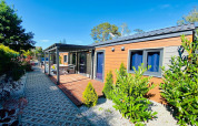 Buitenfoto van een hedendaagse glamping accommodatie met houten terras, tuin en zitbank in de zon.