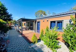 Buitenfoto van een hedendaagse glamping accommodatie met houten terras, tuin en zitbank in de zon.