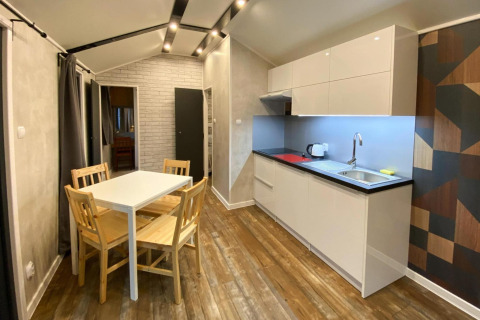 Stijlvolle bungalowkeuken met eetruimte, houten stoelen en witte kasten in Dziwnow, Duitsland.