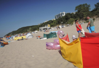 Strandbillede ved Bungalows Pirates i Dziwnow med familier, paraplyer, oppustelig flamingo og klitter.
