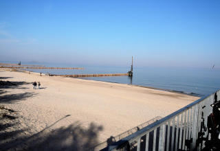 View from At «słonecznikiem» cabin in Germany showing a tranquil sandy beach, calm sea, and clear blue sky.