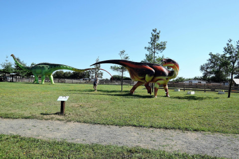 View of an outdoor park in Germany with large dinosaur statues and a person walking between them on grass.