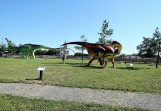 Vista de un parque al aire libre en Alemania con grandes estatuas de dinosaurios y una persona caminando entre ellas.