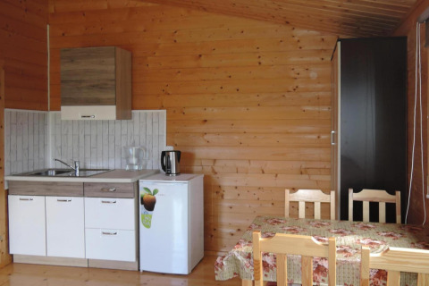 Wood-paneled cabin kitchen and dining area with small kitchenette, mini fridge, and four wooden chairs.