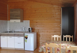Wood-paneled cabin kitchen and dining area with small kitchenette, mini fridge, and four wooden chairs.