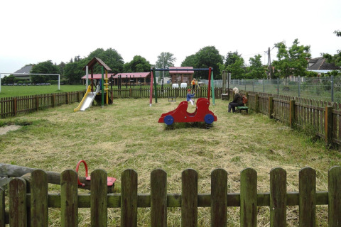 Parque infantil con columpios, tobogán y juegos, cercado, frente a la cabaña At «słonecznikiem» en Alemania.