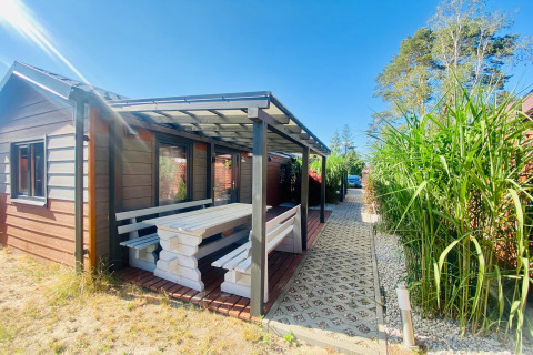 Overdekt terras met picknicktafel bij een glampinghut, omringd door groen en onder een blauwe hemel.