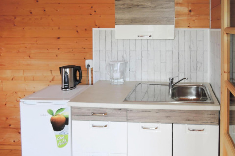 Pequeña cocina con paredes de madera, fregadero, hervidor y nevera en la cabaña At «słonecznikiem» en Alemania.