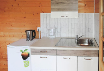 Pequeña cocina con paredes de madera, fregadero, hervidor y nevera en la cabaña At «słonecznikiem» en Alemania.